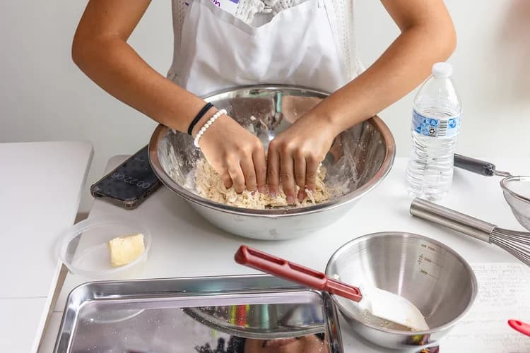 Hands practice a careful culinary technique at a kitchen worktable
